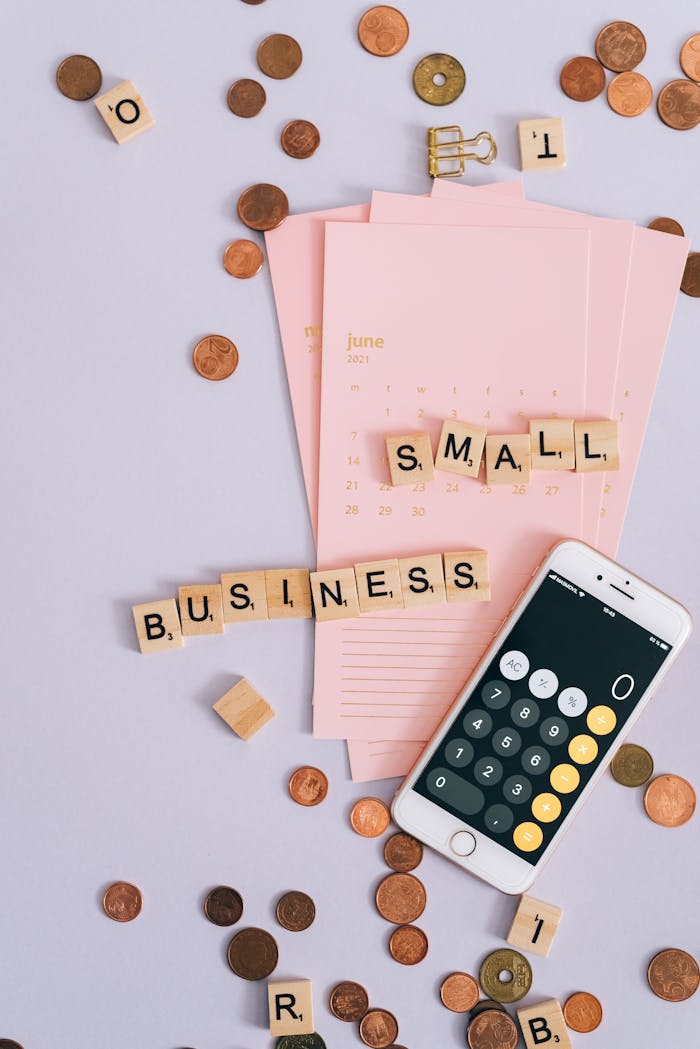 about-02 Flat lay with coins, smartphone, and 'SMALL BUSINESS' tiles on a planner.